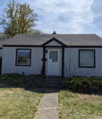 A small white house with a gray roof and a white door.