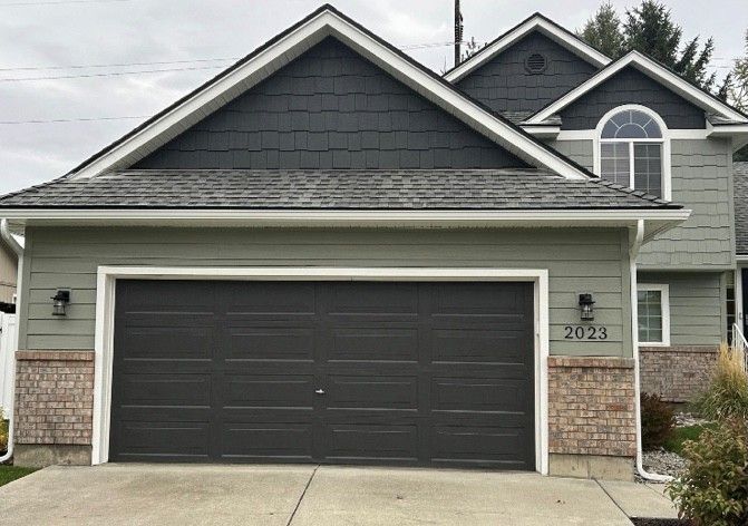 Green house with gray garage door and dark gray roof.