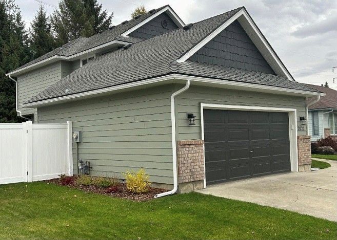 Two-story house with green siding, a dark gray garage door, and a white fence in front.
