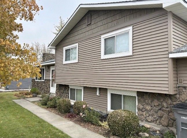 Beige siding house with stone base, white windows, and green lawn.
