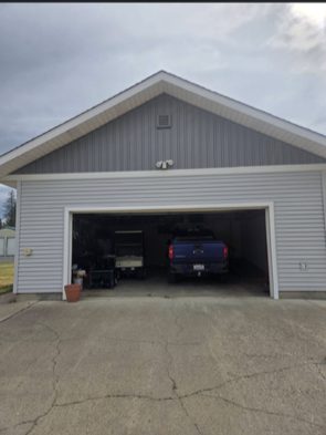 A light gray detached garage with a dark blue pickup truck and a small utility vehicle parked inside.