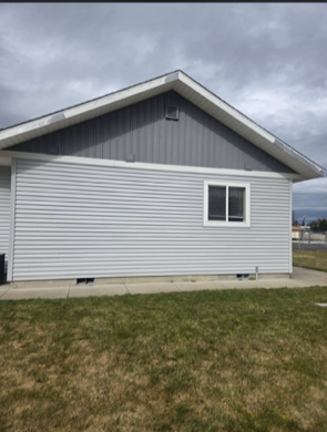 Side view of a house with light grey horizontal siding, dark grey vertical gable siding, white trim, and a window.