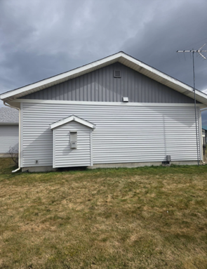 The side of a house with light grey siding, a dark grey triangular gable, and a small, protruding utility enclosure.