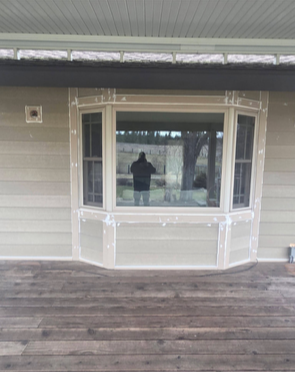 Exterior view of a house with a bay window and a person reflected in the glass.