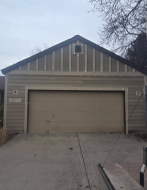 Tan garage with brown door and roof, concrete driveway. Cloudy day.