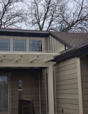 House exterior with pergola, windows, and brown siding under a cloudy sky.