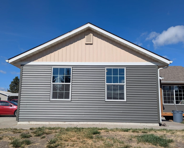 A small house with gray siding and two windows