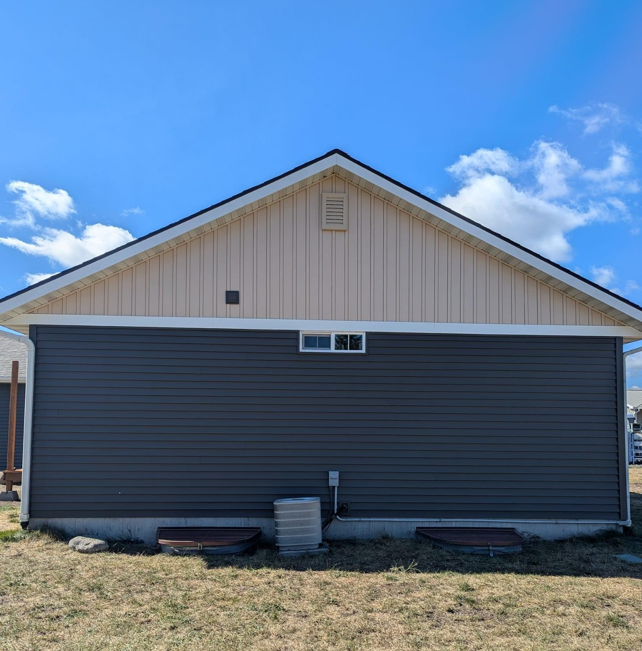 A house with a gray siding and a white roof is sitting in the middle of a grassy field.