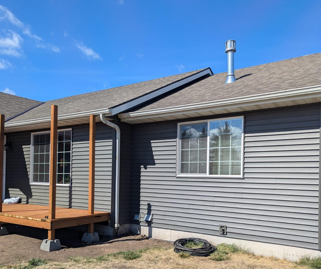 A gray house with a wooden deck and a chimney on the roof.