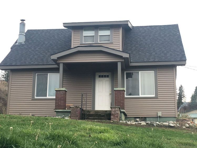 A brown house with a black roof and a porch