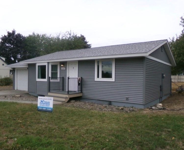 A small gray house with a sign in front of it.