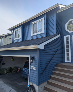 A blue house with a car parked in the garage and stairs leading up to it.