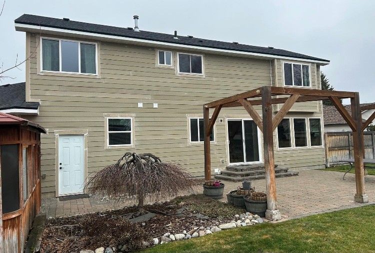 Back of a two-story beige house with a wooden pergola, sliding glass door, and a small yard on a cloudy day.