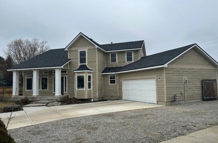 Two-story beige house with white columns, a garage, and a long driveway under a cloudy sky.