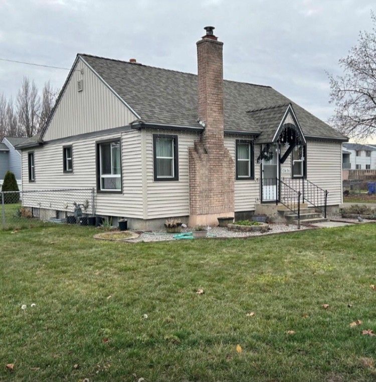 Beige house with a brick chimney, gray roof, and black-framed windows; front lawn.