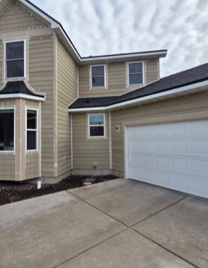 Tan two-story house with white garage door and concrete driveway on a cloudy day.
