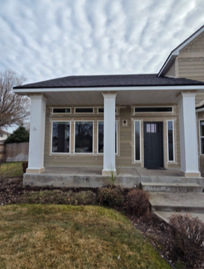 Tan house with white columns, windows, and dark front door under a cloudy sky.