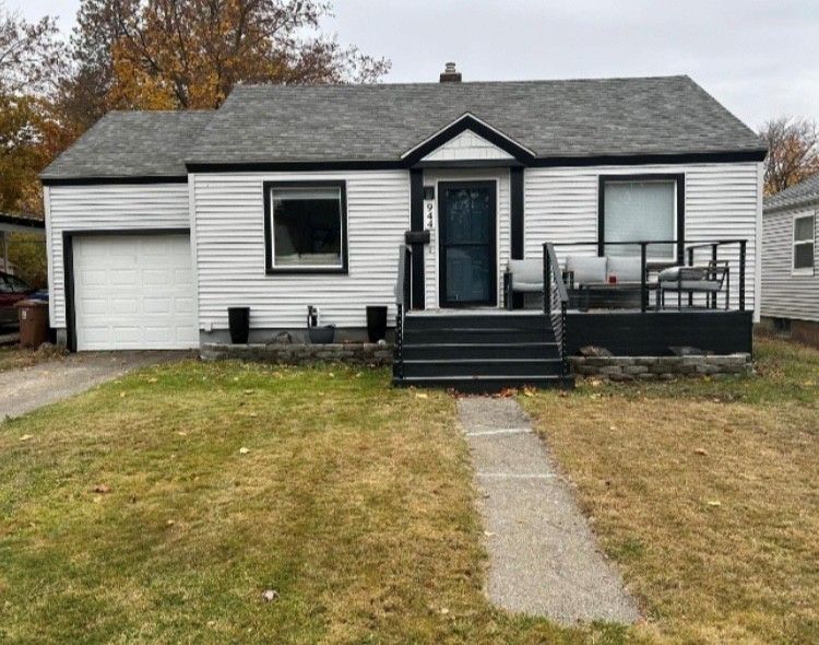 White bungalow house with black trim, small porch, and garage door on a grassy lawn.