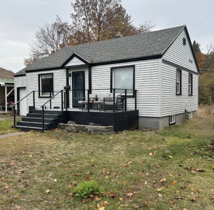 White clapboard house with black trim, porch, and steps on a grassy lot.