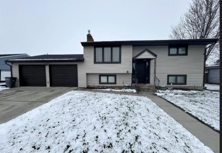 Two-story house with black garage doors, snow-covered yard, and gray siding on an overcast day.