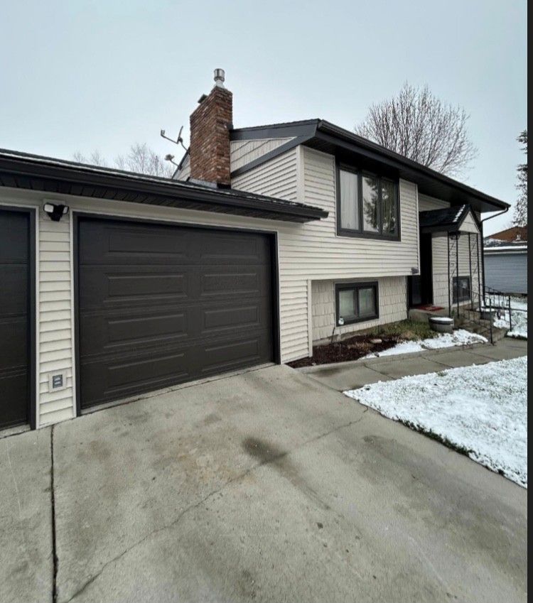 Beige house with brown garage doors and a brick chimney, snowy driveway.