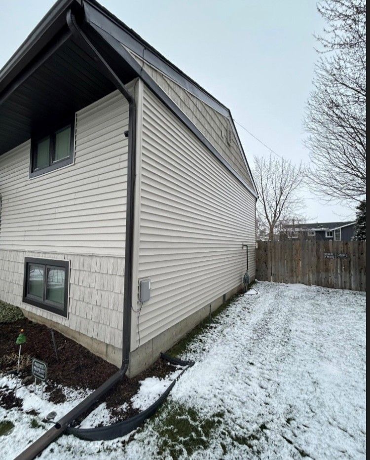 Side view of a two-story beige house with dark trim and a snowy yard.