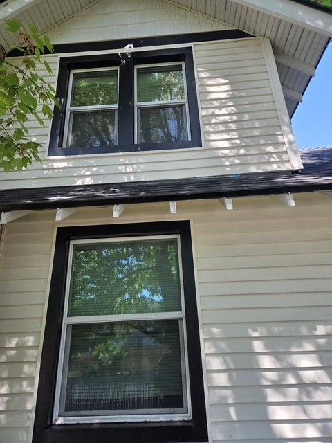 Two black-trimmed windows on a white house exterior beneath a steep gabled roof