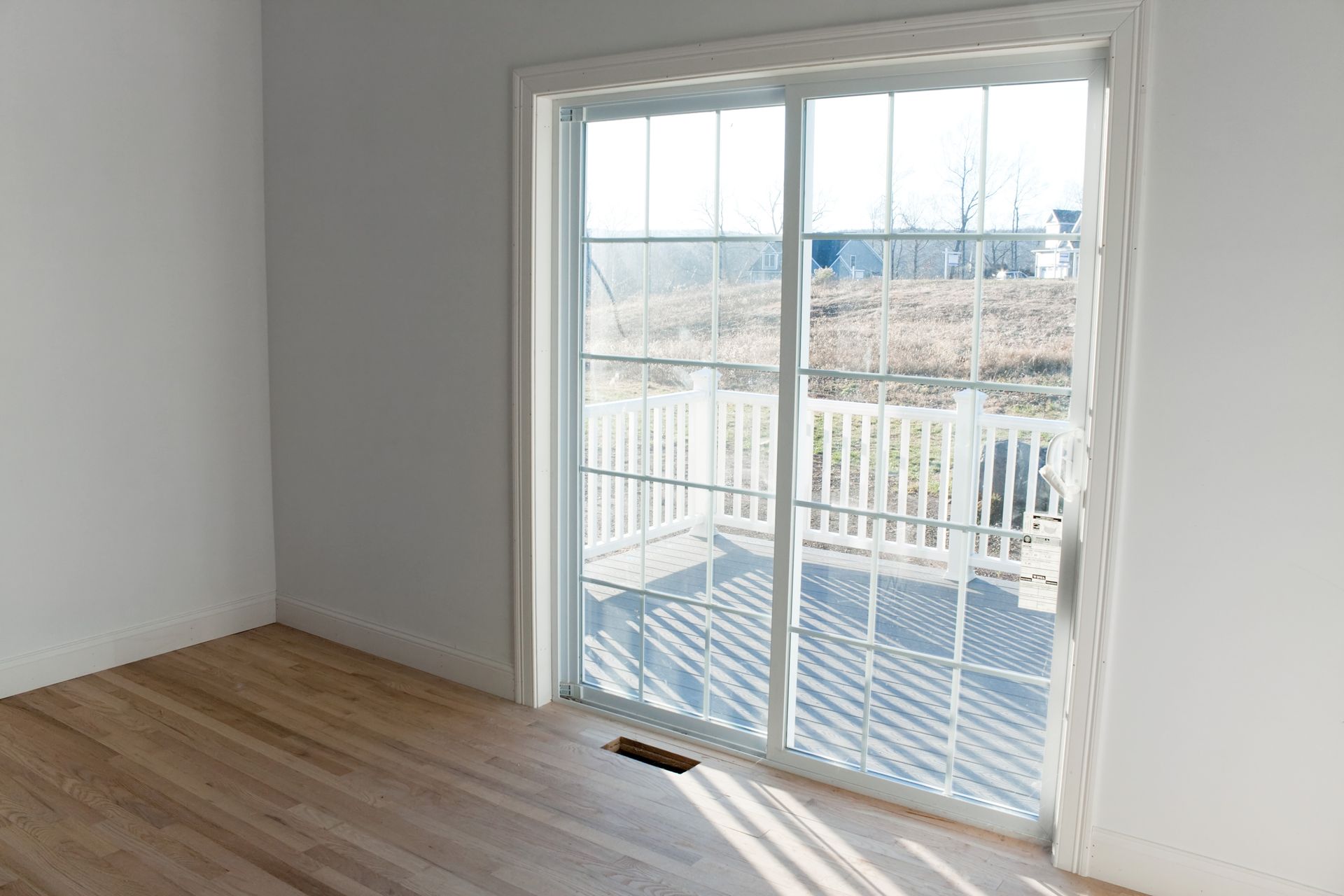 Sunlit room with a white sliding glass door leading to a wooden deck and open yard view.