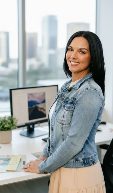 Woman in denim jacket smiling by desk in office.