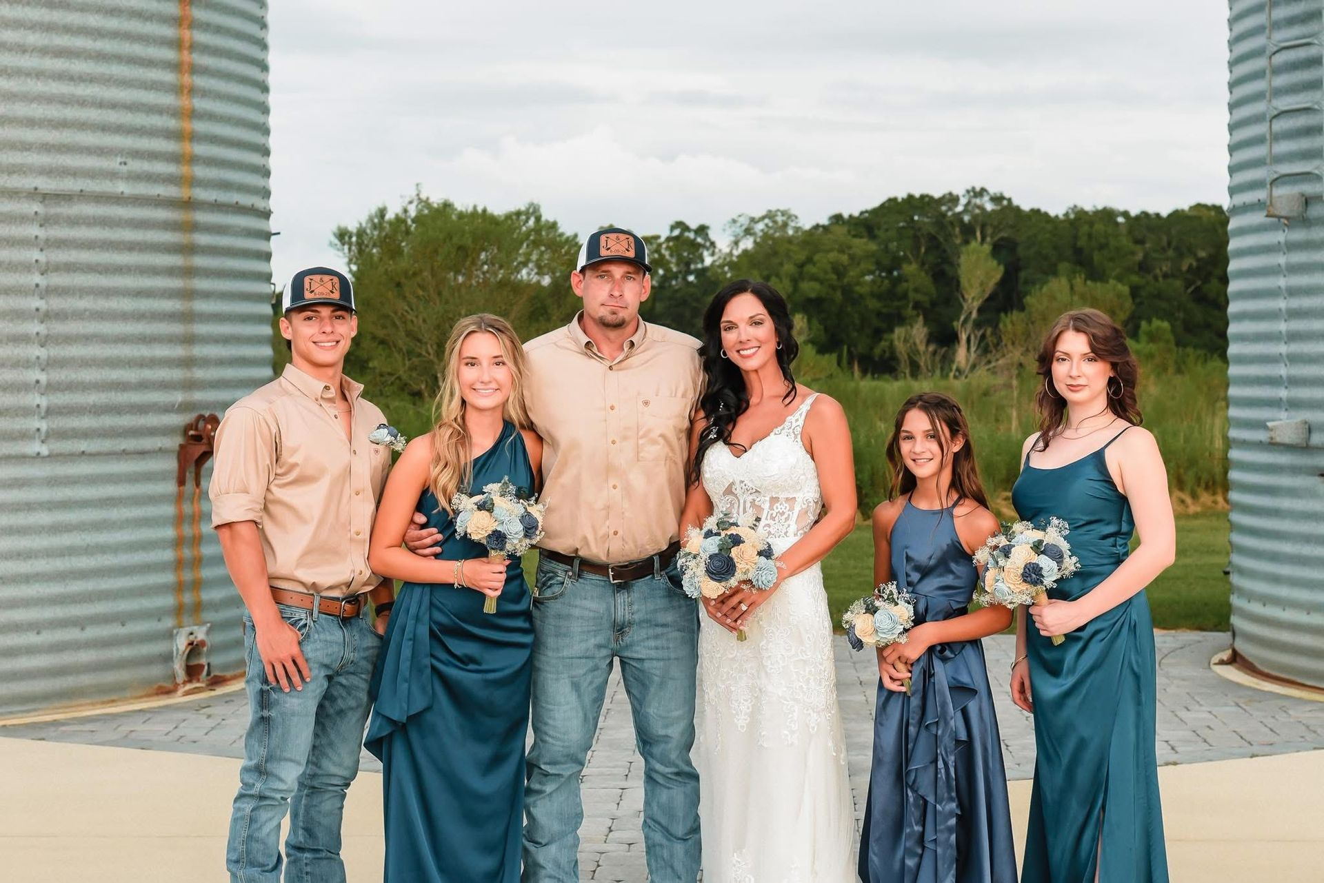 Wedding party posing. Bride in white dress, groom, bridesmaids in teal, setting: outdoor farm.