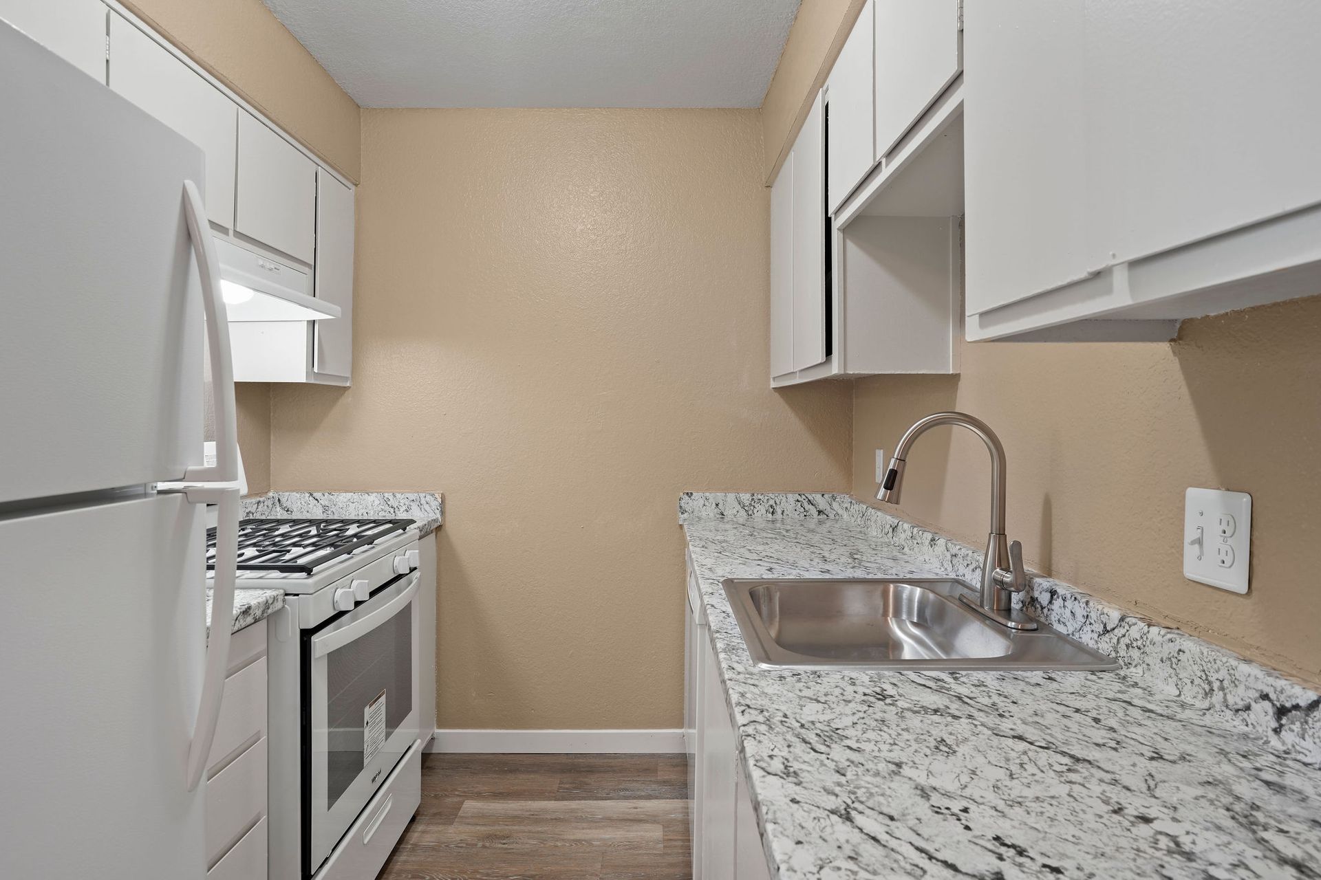 Narrow modern kitchen with white cabinets, granite counters, stainless sink, and white appliances.