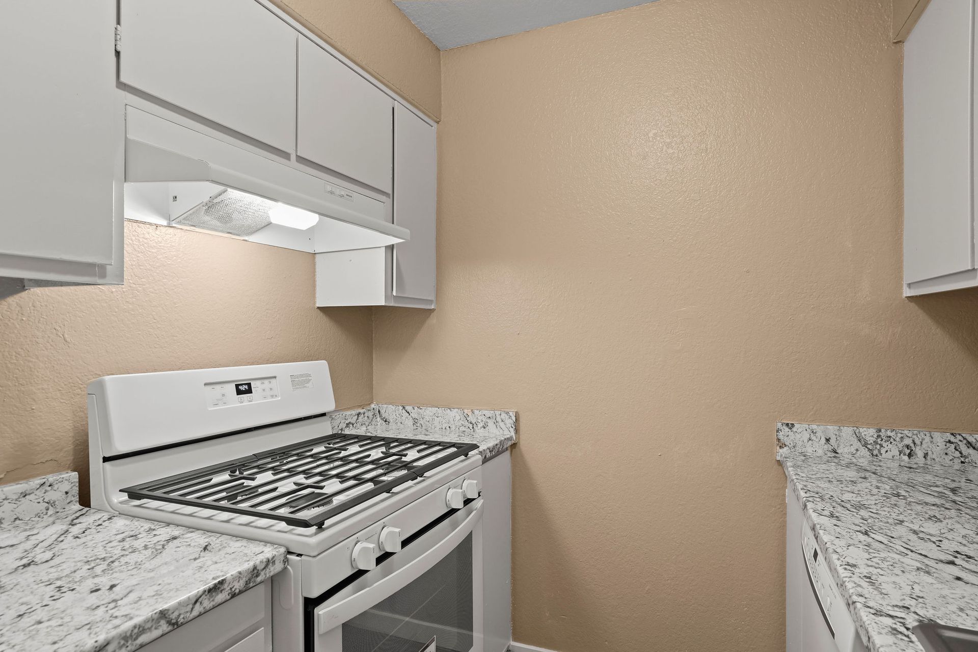 Small kitchen with white stove, beige walls, and speckled countertops on both sides