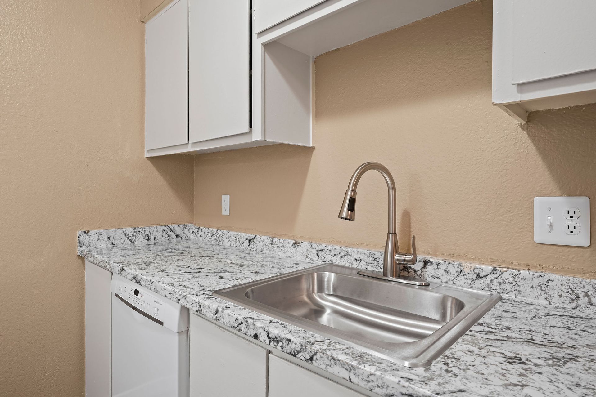 Small kitchen with white cabinets, granite countertop, and stainless steel sink and faucet against beige walls