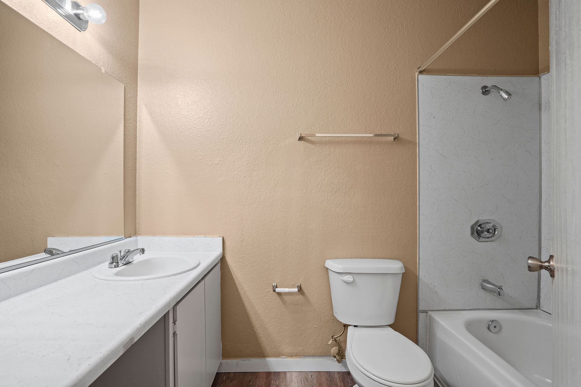 Small beige bathroom with a sink, toilet, and bathtub with glass shower door.