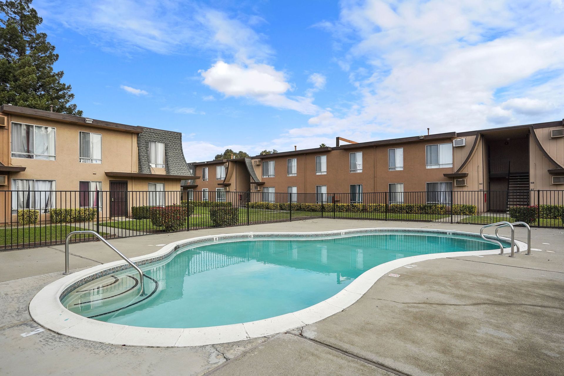 Outdoor apartment pool with turquoise water and tan townhouse buildings under a blue sky