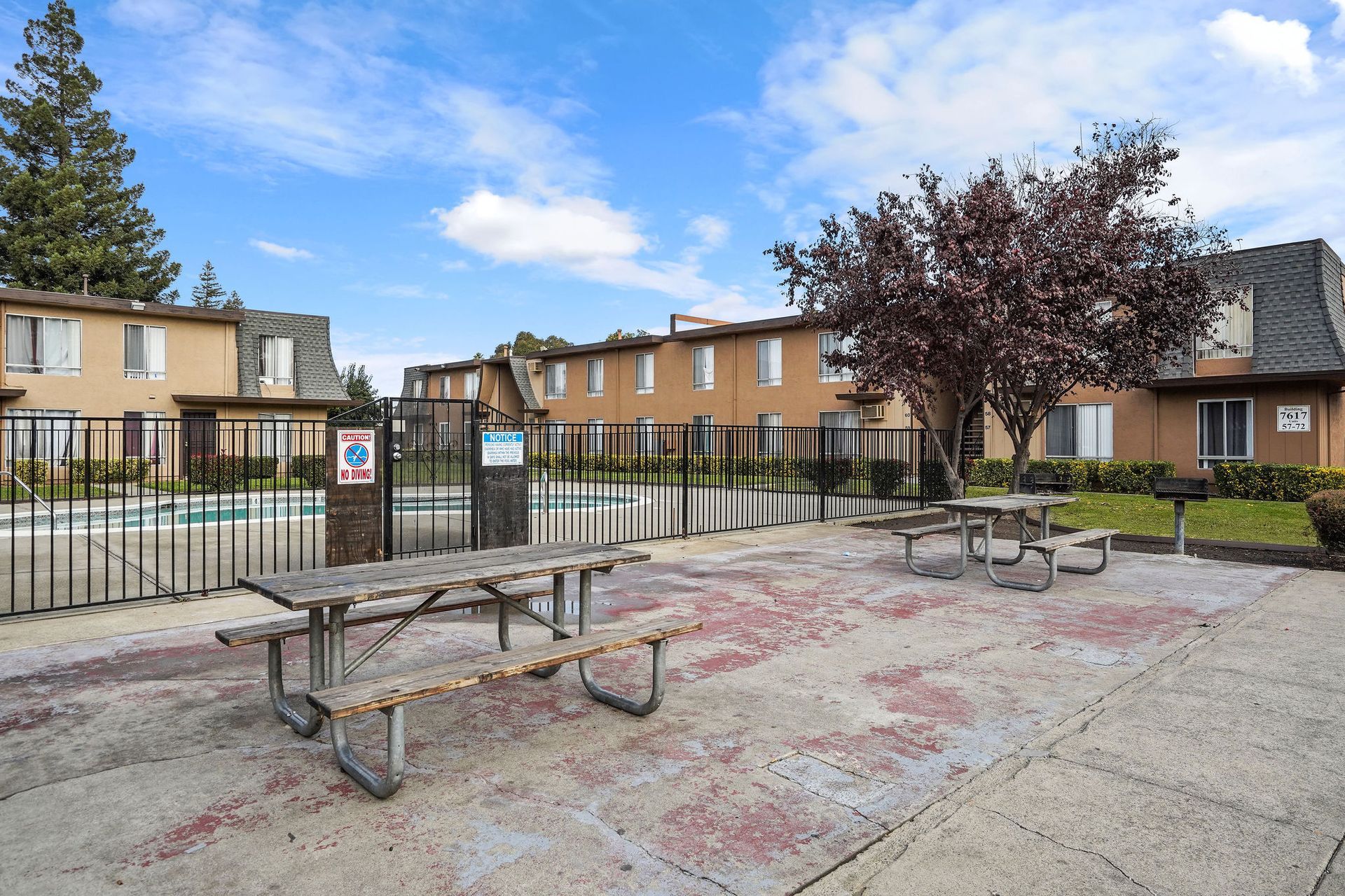 Courtyard with picnic tables, black fence, and apartment buildings under a partly cloudy sky