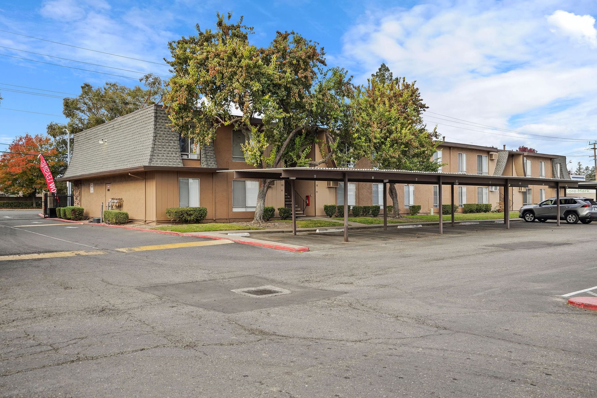 Motel parking lot with low tan buildings, trees, and several parked cars under a covered walkway