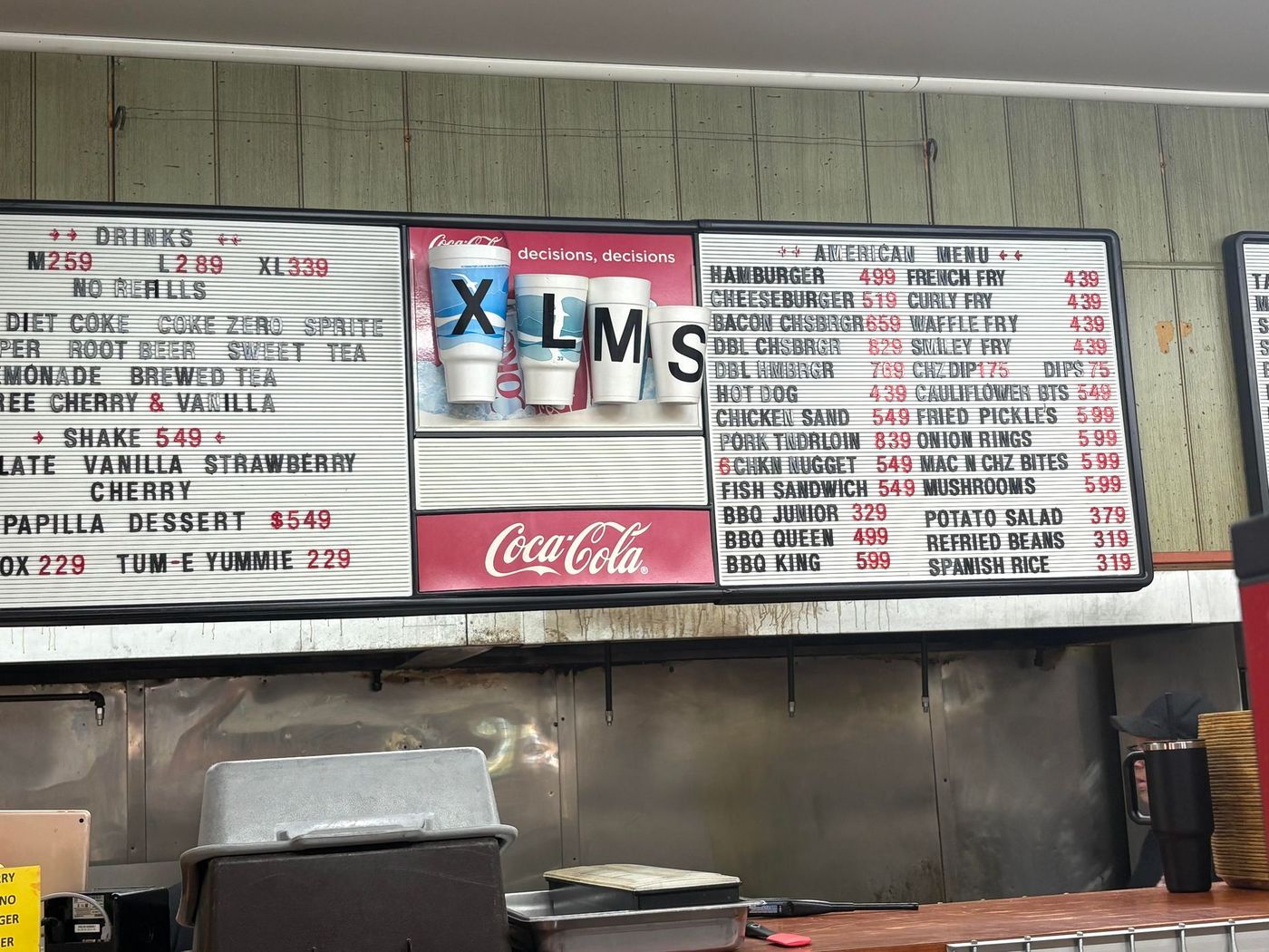 Menu board with drink sizes (XL, M, S) and food options, Coca-Cola logo.