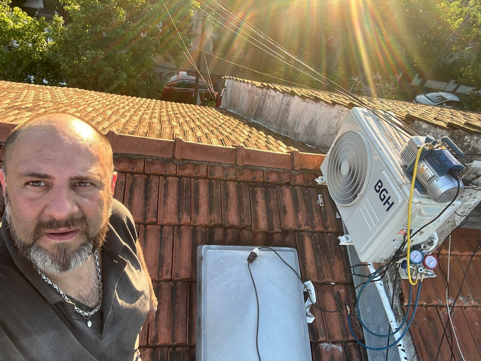 Un hombre posa junto a una unidad de aire acondicionado en un tejado de tejas bajo la luz del sol.