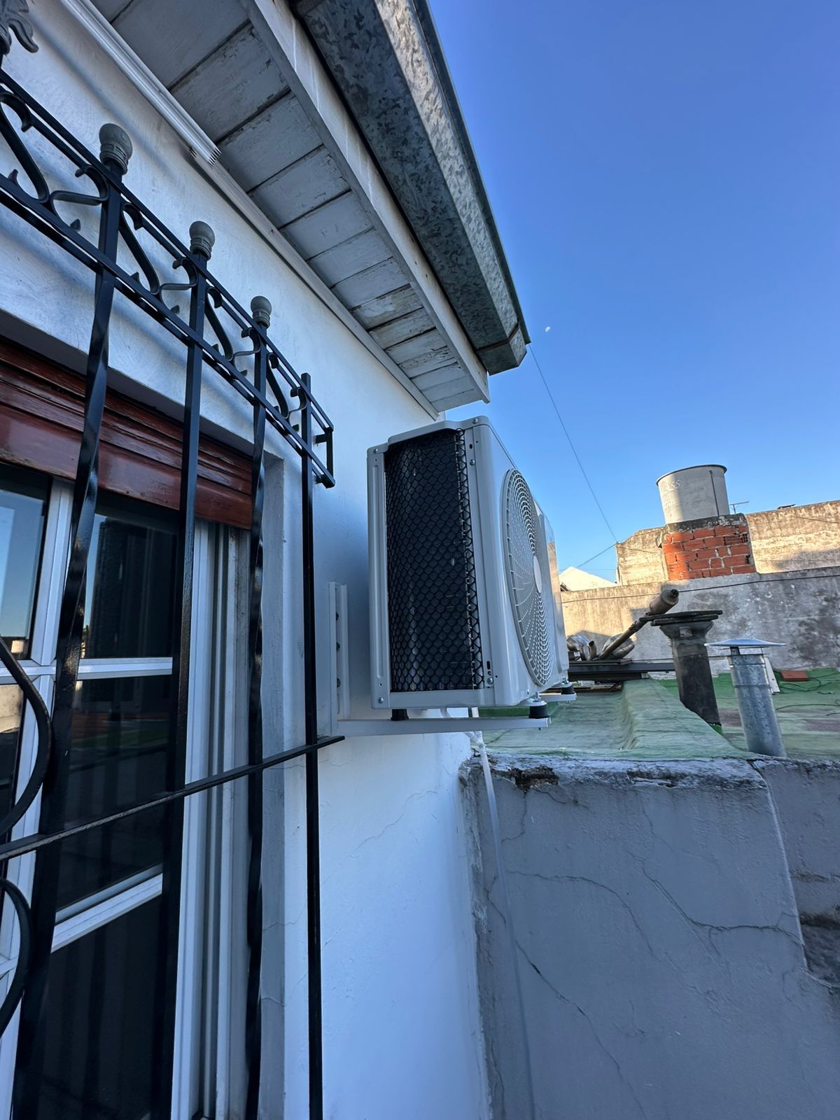 Unidad de aire acondicionado exterior montada en la pared blanca de un edificio con fondo de cielo azul.