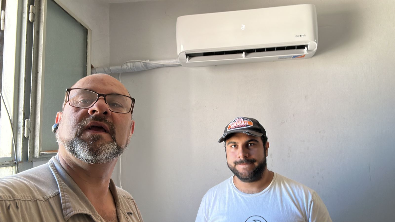 Dos personas con gafas de seguridad inspeccionan tuberías rojas en un edificio de ladrillo y hormigón.