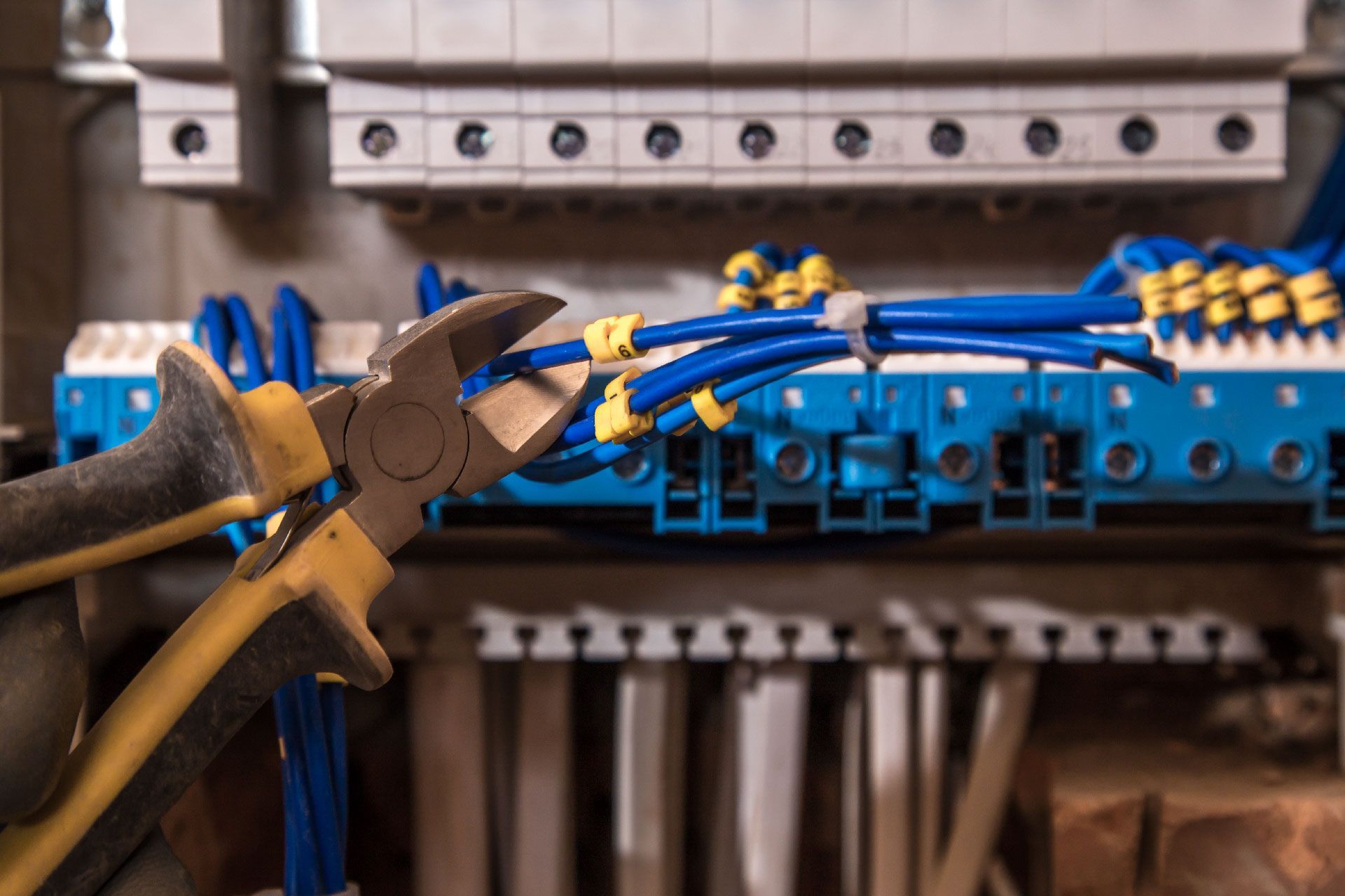 Mano enguantada de electricista utilizando alicates de corte en cables eléctricos azules en un panel de circuitos.