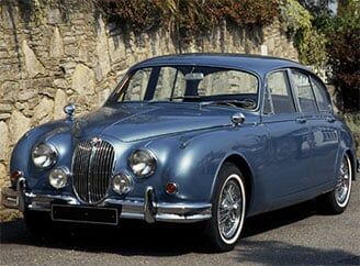 A blue jaguar car is parked in front of a stone wall.