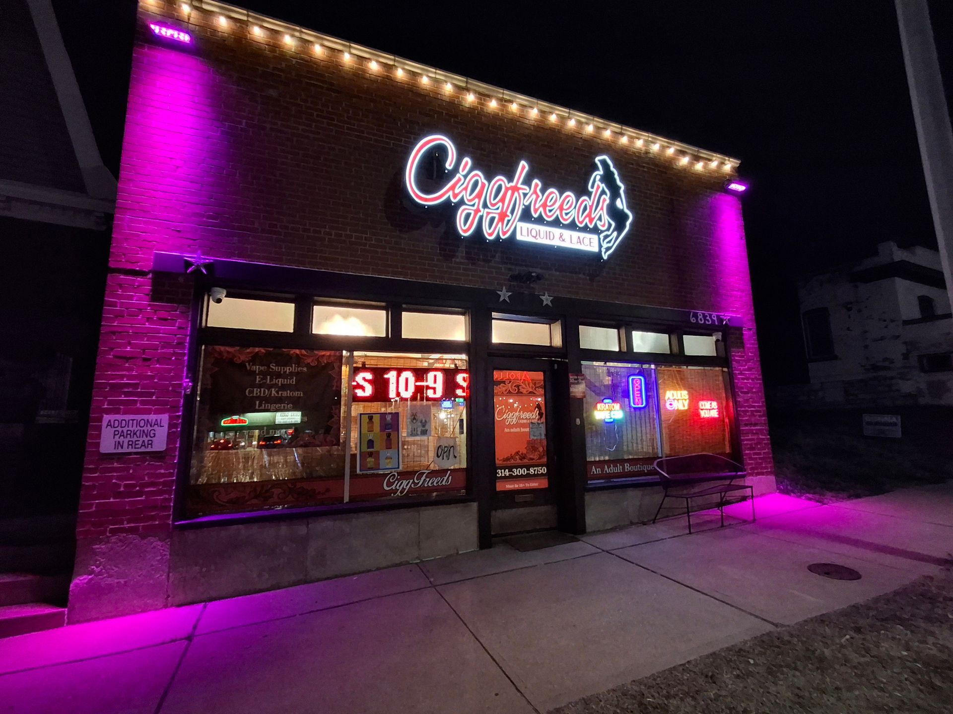 A brick storefront at night, illuminated by bright pink accent lighting, with a sign reading