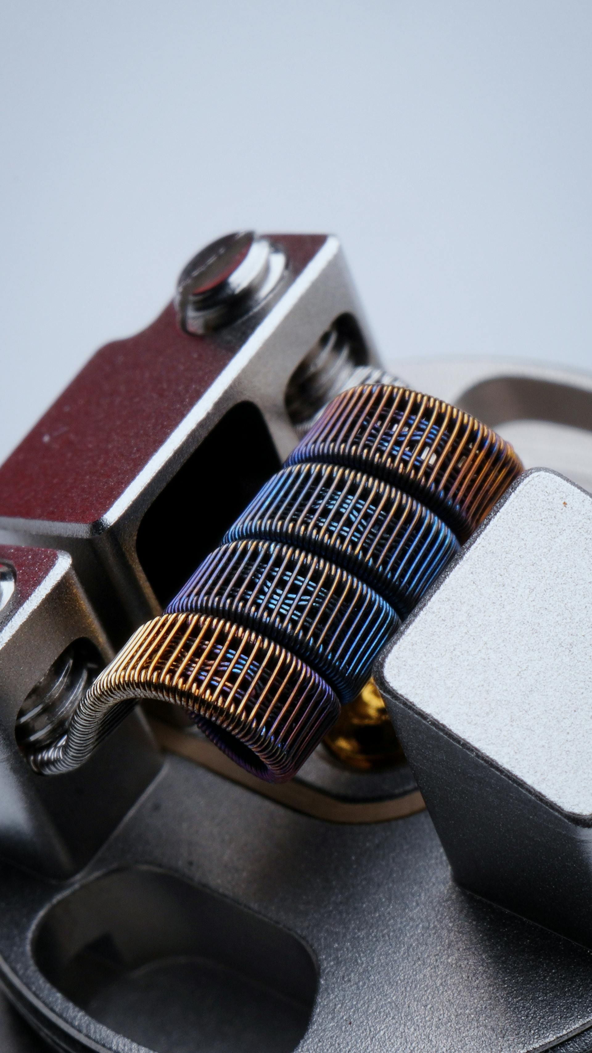 A colorful, metallic heating coil for an electronic cigarette, installed in a grey atomizer deck.