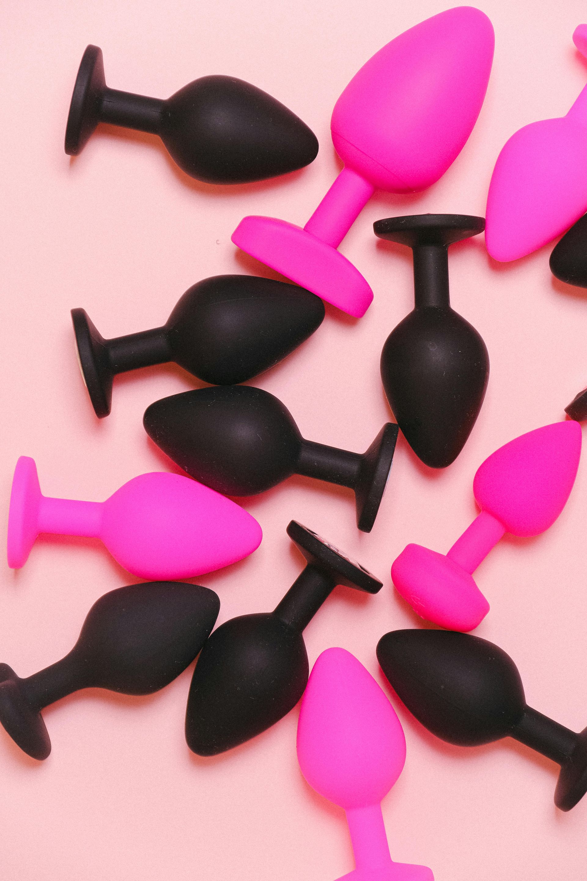 A flat-lay view of several small, bulb-shaped silicone plugs in alternating black and bright pink colors.
