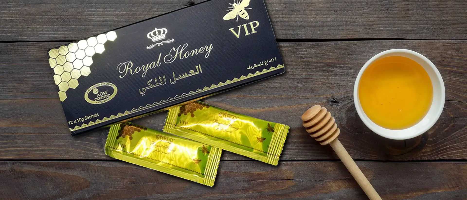 VIP Royal Honey box and individual gold packets next to a small cup of honey and a wooden dipper on a wooden surface.