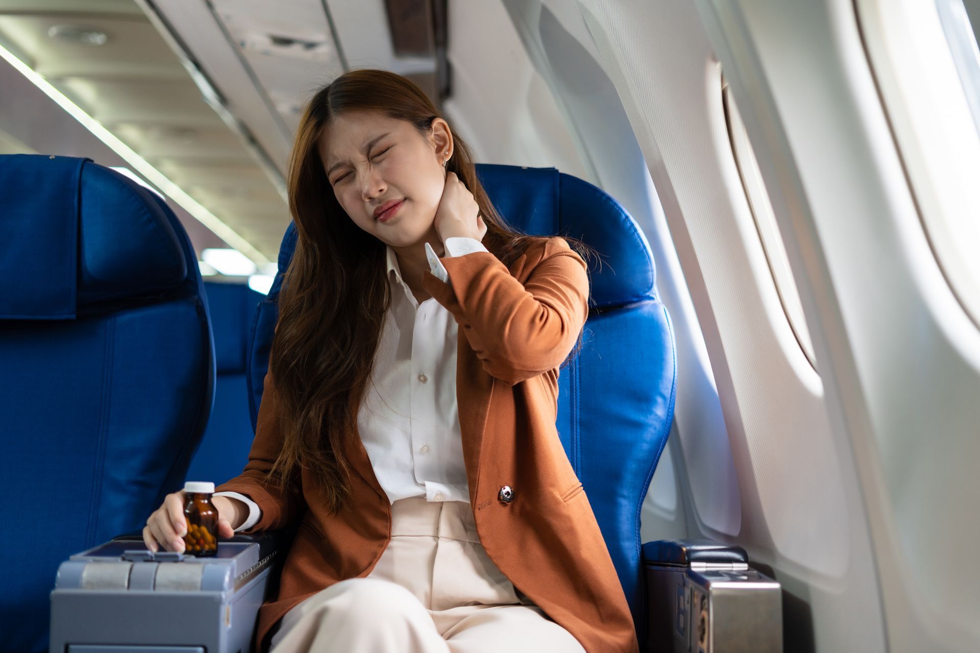 A woman is sitting on an airplane with a bottle of pills in her hand.