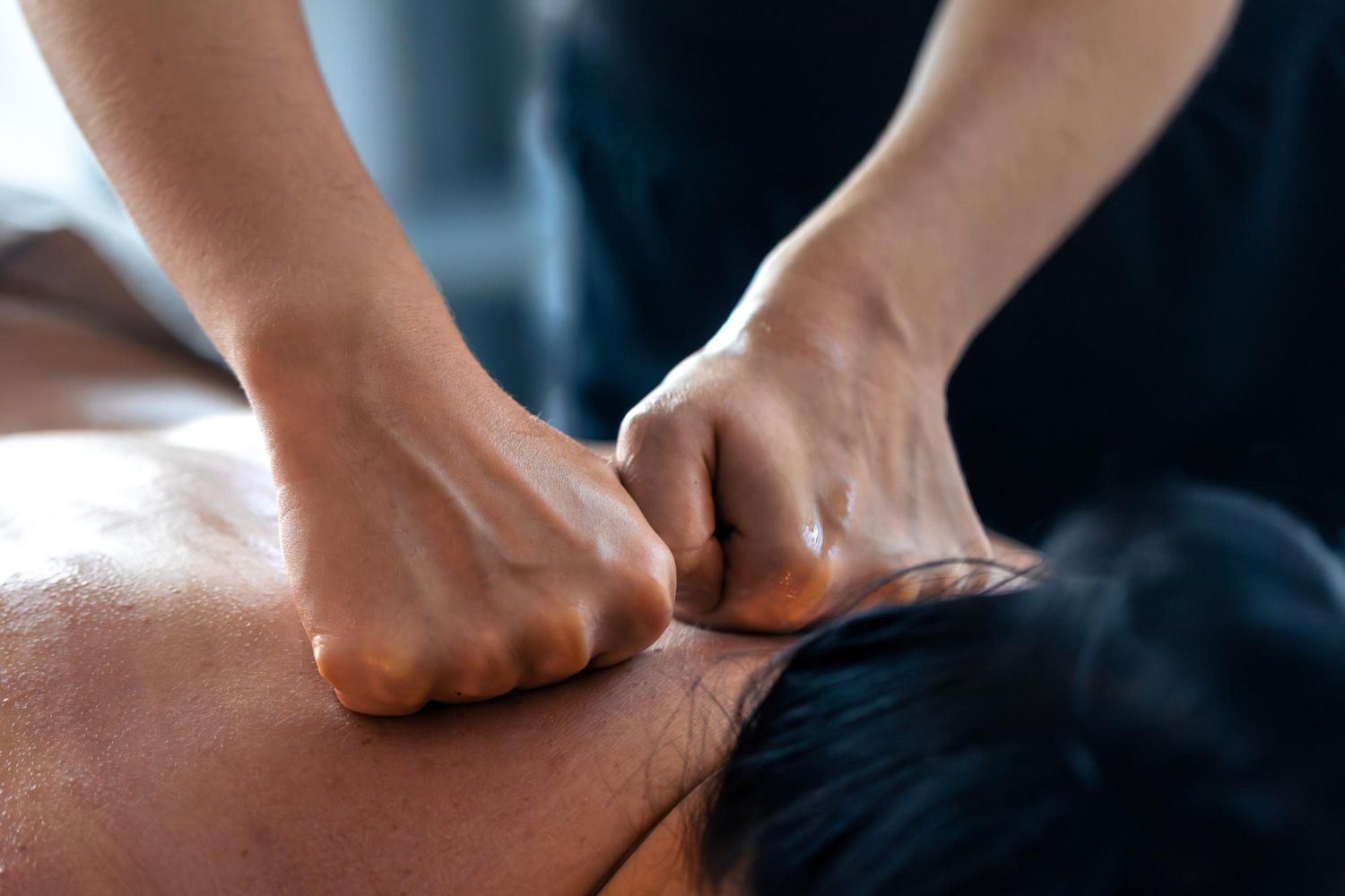 Hands massaging neck and back of a person, likely for therapeutic purposes.