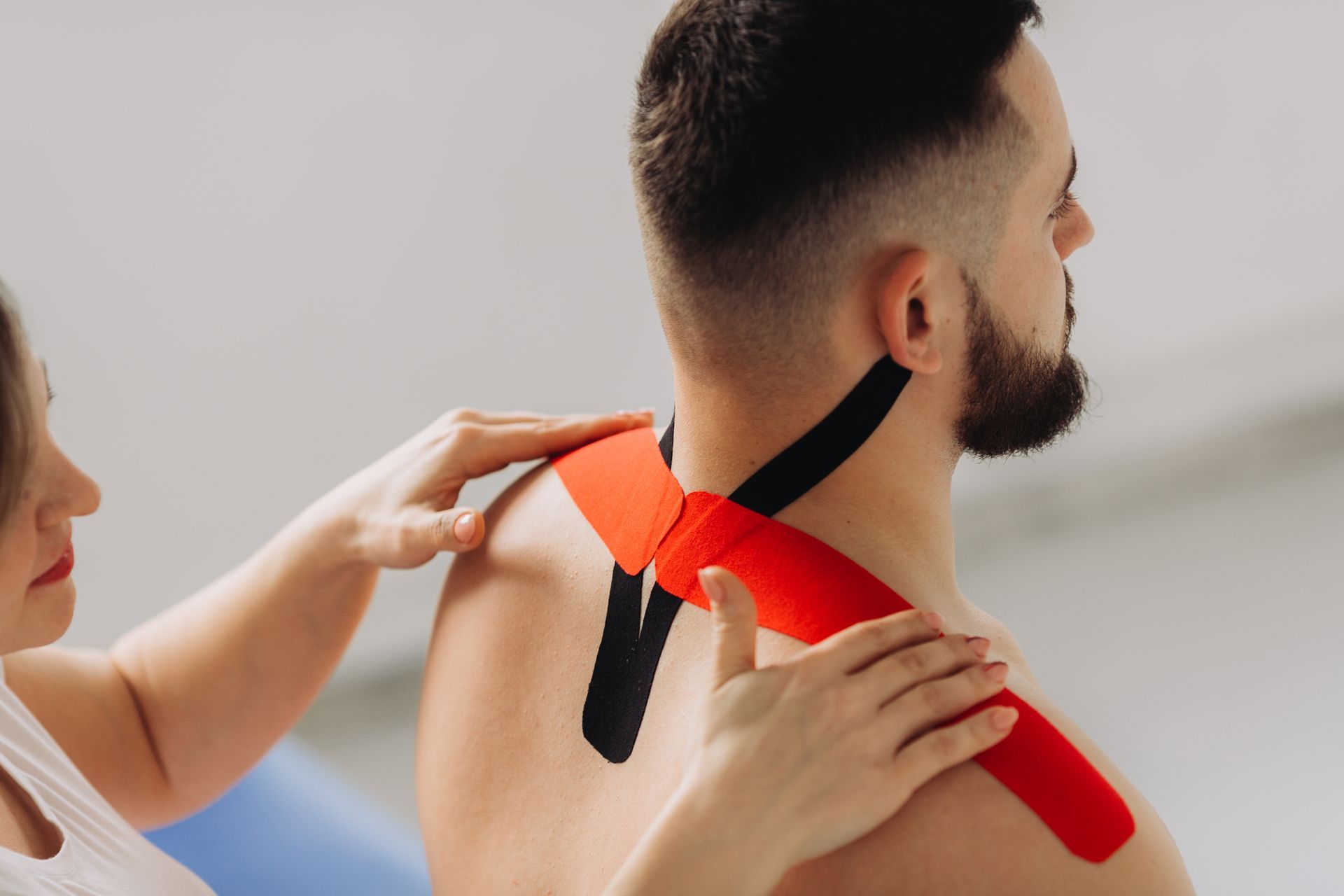 A woman is putting kinesio tape on a man 's neck.